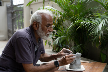 Indian old man crafting an eco-friendly clay Ganesh idol for Ganesh Chaturthi and teaching kids how to do it, sitting outdoors in a garden
