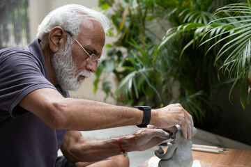 Indian old man crafting an eco-friendly clay Ganesh idol for Ganesh Chaturthi and teaching kids how to do it, sitting outdoors in a garden
