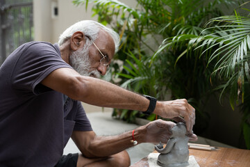 Indian old man crafting an eco-friendly clay Ganesh idol for Ganesh Chaturthi and teaching kids how to do it, sitting outdoors in a garden
