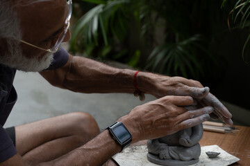Indian old man crafting an eco-friendly clay Ganesh idol for Ganesh Chaturthi and teaching kids how to do it, sitting outdoors in a garden
