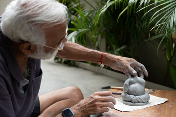 Indian old man crafting an eco-friendly clay Ganesh idol for Ganesh Chaturthi and teaching kids how to do it, sitting outdoors in a garden
