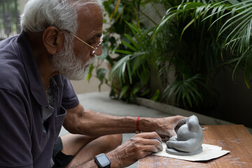Indian old man crafting an eco-friendly clay Ganesh idol for Ganesh Chaturthi and teaching kids how to do it, sitting outdoors in a garden
