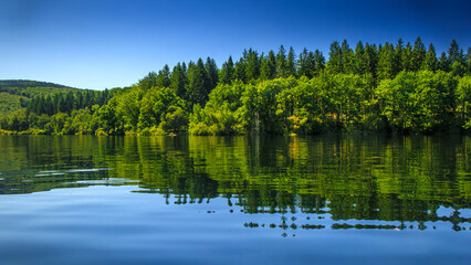 Obraz premium Landscape of Lake La Ravière in the early morning in the South of France. Calm water surrounded by forest in Occitanie.