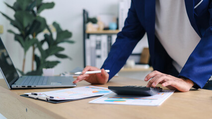 Businessman analyzing financial charts with calculator and laptop at office desk. Concept of accounting, investment planning, corporate finance, and data analysis.