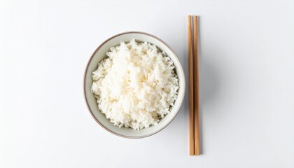 Overhead shot of a bowl filled with fluffy white rice, accompanied by a pair of wooden chopsticks on a white background.