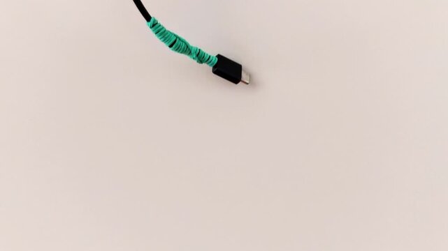 Minimalist frame featuring a black cable with green wrap, suspended against a white backdrop. A quiet study in contrast, texture, and modern simplicity