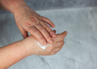 An old, elderly woman smears her hands with cream. Background and texture