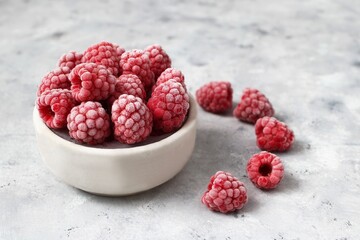 Frozen Raspberries in Bowl and Scattered on a Textured Gray Surface. Healthy Eating Concept.