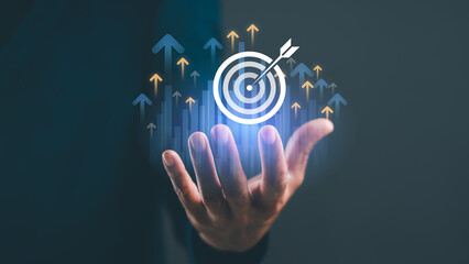 A hand holds a target symbol with arrows indicating growth, representing focus, goals, and success in business or personal development.