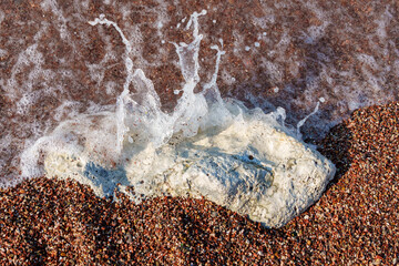 big beautiful white stone lies on coastline and small stones of beach of Adriatic Sea, with beautiful foaming wave, as abstract background of summer travel and vacation