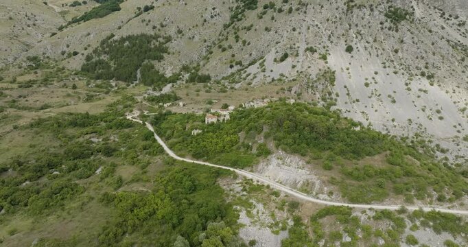 Aerial view of the ancient Frattura Vecchia ruins, nestled between verdant hills and rocky mountains, creating a mesmerizing contrast, Frattura Vecchia, Abruzzo, Italy.