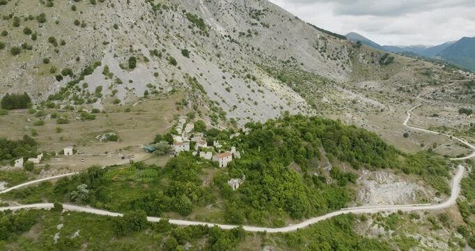 Aerial view of Frattura Vecchia showing buildings nestled amongst verdant trees beneath a towering mountainside, creating a striking contrast, Frattura Vecchia, Abruzzo, Italy.