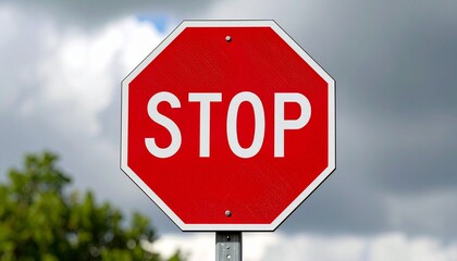 Obraz premium Red octagonal stop sign outdoors with white text, green foliage and cloudy sky background