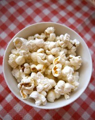 Fresh popcorn in a white bowl placed on a red checkered napkin with copy space.