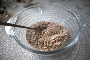 Dry oatmeal and cocoa powder in a transparent glass bowl, close-up view.