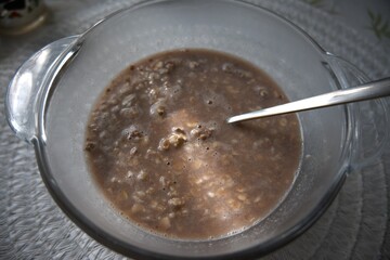 Chocolate flavored oatmeal powder prepared with water in a clear glass bowl, close-up.
