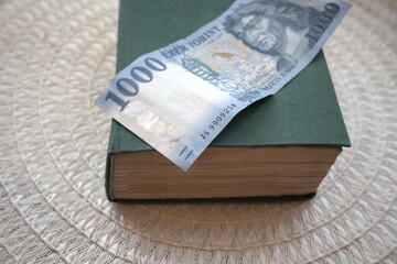 Hungarian 1000 forint banknote placed on a green book symbolizing the value of knowledge.