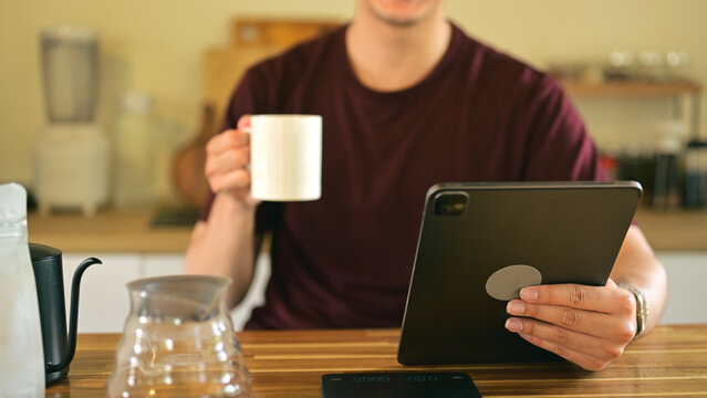Close up of a man holding a coffee mug while using digital tablet in the kitchen