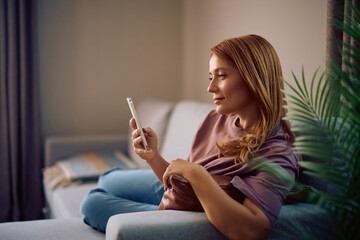 Smiling woman using cell phone while relaxing on sofa.