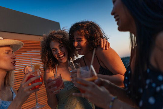 Friends laughing and drinking cocktails at sunset rooftop party
