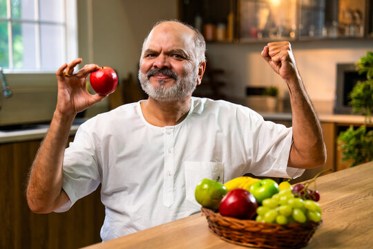 Indian Old man enjoying apple and urging healthy eating from home kitchen