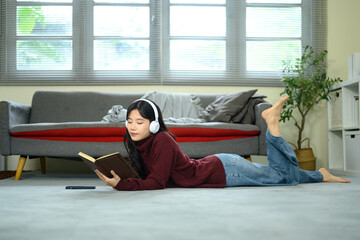 Young woman lying on the floor with headphones, enjoying a book in a living room