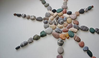 A symbol of the sun with rays, laid out from smooth sea pebbles on a white surface
