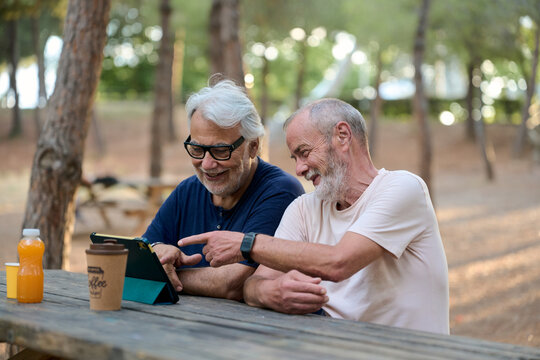 Two senior men using a tablet in a park, sharing moments and staying connected - Powered by Adobe