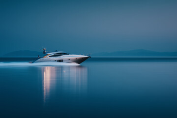 Luxury white yacht cruising smoothly on calm blue waters at dusk with distant mountains in the background
