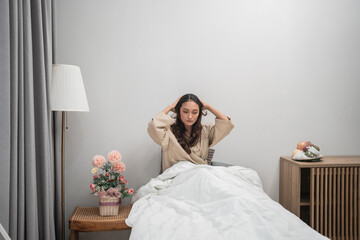 Fototapeta premium A woman appears to be feeling stressed while sitting in a cozy and warm bedroom environment
