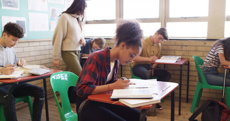 Writing, test and teacher walking in classroom for assessment, exam and quiz supervision. High school, academy and woman with students with assignment for education, learning and lesson progress