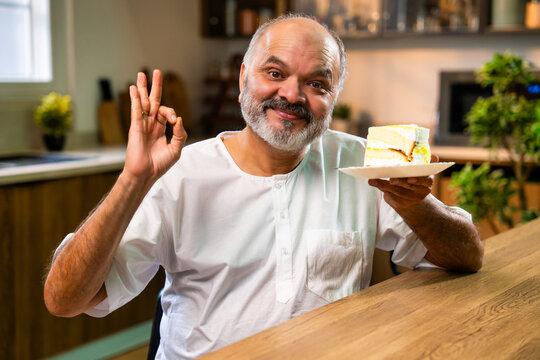 Elderly Indian man hiding while eating sweet pastry at home