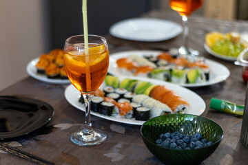 Inviting dinner party with assorted avocado & salmon sushi rolls, vibrant orange cocktails, and fresh blueberries in a green bowl, all laid out on a table.