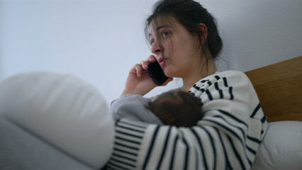 Mother talking on the phone while her newborn sleeps soundly in her arms, conveying a mix of exhaustion and dedication. the quiet moments of balancing rest and responsibility