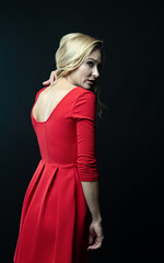Fototapeta premium Elegant blonde woman posing in red dress on black background 