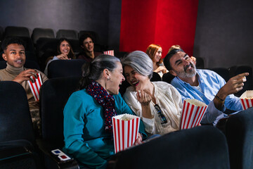 Multi ethnic group of friends laughing and eating popcorn while watching a comedy movie at the...