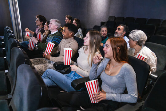 Group of diverse friends enjoying a movie at the cinema, eating popcorn and having fun together