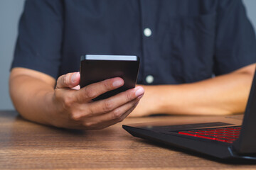Hand holding smartphone next to laptop on desk.