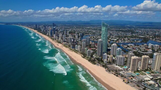 A breathtaking aerial view of Gold Coast, Australia, showcasing the stunning coastline, high-rise skyline, and beautiful sandy beaches. The turquoise ocean waves crash along the shore