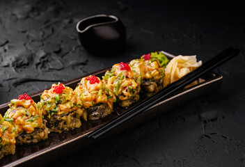 Delicious sushi rolls on a black plate with wasabi and ginger garnish