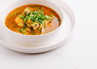 Delicious seafood soup garnished with fresh herbs on a white plate