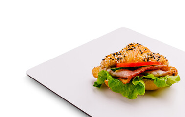 Fresh croissant sandwich with lettuce, ham, and tomato on a white plate