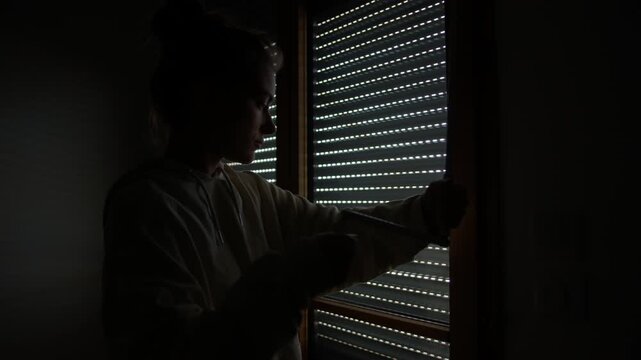 Close up of woman closing blind integrated into window using crank mechanism