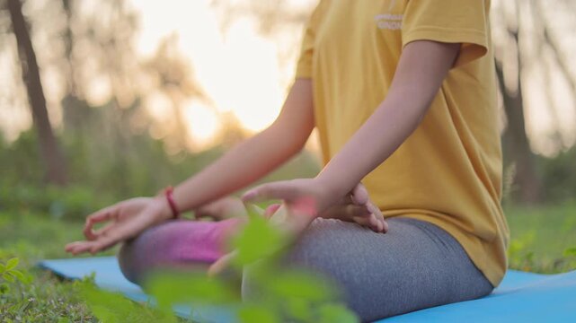 Close up shot of a woman sitting in lotus position on a yoga mat at outdoor during golden hour.