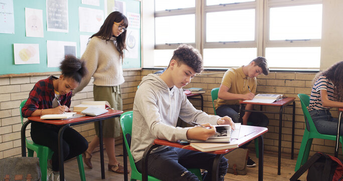 Test, high school and teacher walking in class for assessment, exam and quiz supervision. Teaching, academy and woman with students writing assignment for education, learning and lesson progress