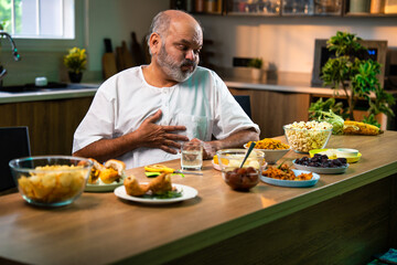 Elderly Indian man drinks antacid in modern kitchen after eating