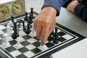 Male hand makes a careful move with a white piece on a busy chessboard; strategy, thinking and...