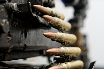 Belt of brass rounds feeds into a scratched, worn automatic gun; copper tips and steel links show...