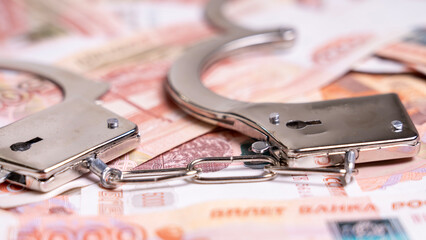 Two handcuffs are on top of a pile of money. The handcuffs are silver and appear to be brand new....