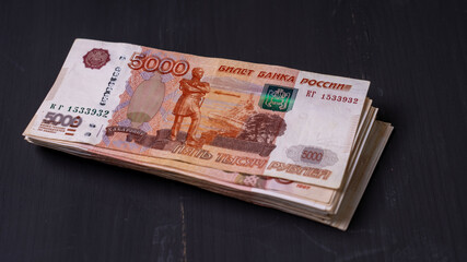 A stack of Russian banknotes with the number 5000 on them. The banknotes are piled on top of each other on a dark surface